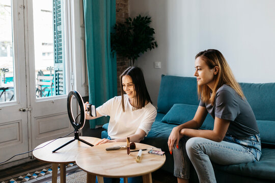 Female influencer vlogging by girlfriend sitting on sofa at home