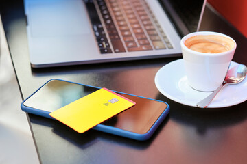 credit card on smart phone by coffee cup and laptop at sidewalk cafe