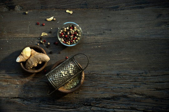 Bowls with ginger root, old grater and various peppercorns lying on wooden surface