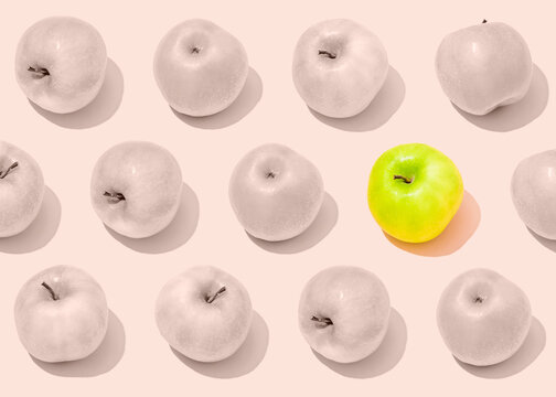 Pattern of rows of bland light pink apples with single vibrant green one