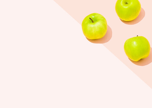 Studio shot of three green apples lying against light pink background