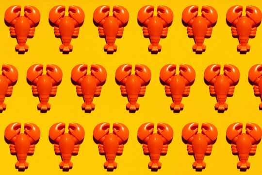Pattern of rows of plastic lobsters flat laid against yellow background