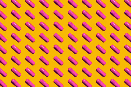 Pattern of rows of pink medicine capsules laid against yellow background