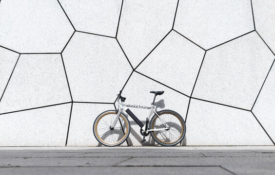 Fixie bicycle on footpath in front of white wall during sunny day