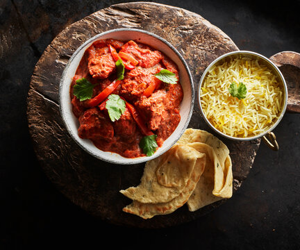 Studio shot of bowl of chicken tikka, bowl of basmati rice and naan bread