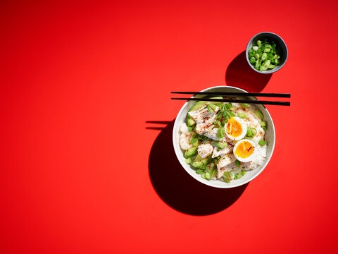 Studio shot of bowl of congee with chicken breasts, boiled egg, avocado and scallions