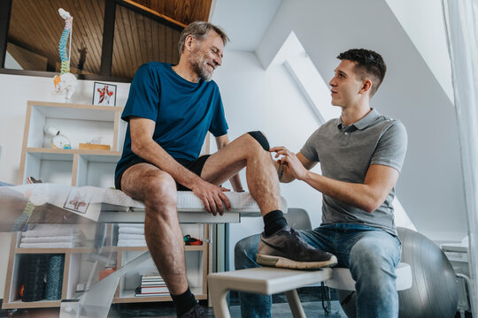 Male physiotherapist looking at smiling patient while sticking elastic therapeutic tape in practice