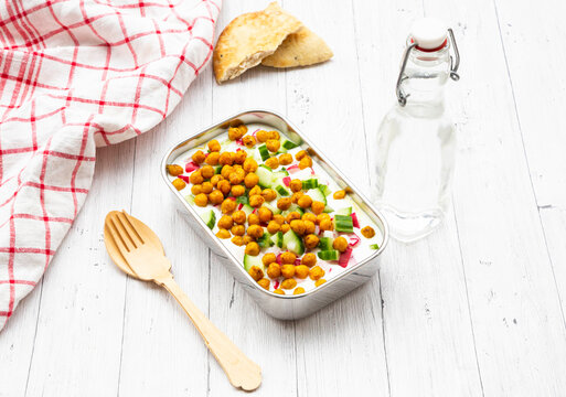 Studio shot of bottle of water, napkin, wooden cutlery,&nbsp;flatbread&nbsp;and lunch box of yogurt with chick-peas, cucumbers and radishes