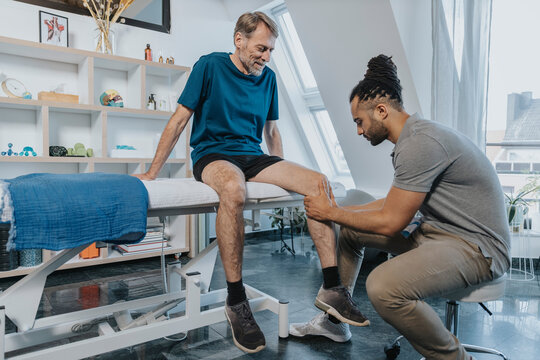 Male physiotherapist checking out knee of patient in practice