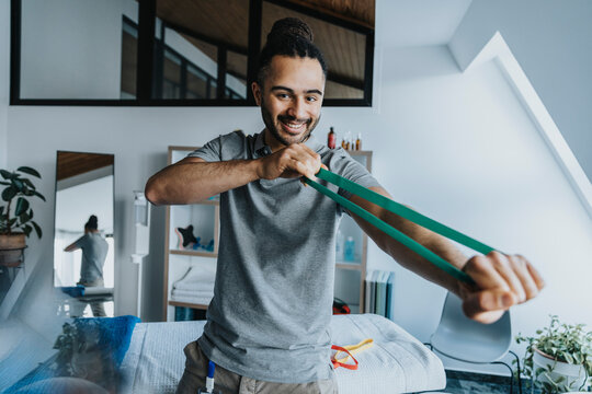 Smiling male physical therapist stretching resistance band in practice