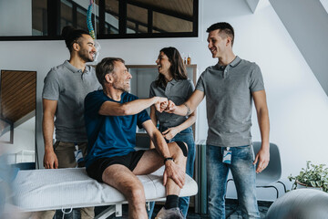Male patient punching fists with physiotherapist standing by colleagues in practice