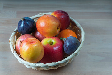 ripe delicious apricots, apples and figs in a wicker basket on a wooden background