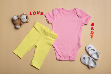 Close-up top view. Mockup blank pink bodysuit, yellow pants and white newborn sandals on a beige...