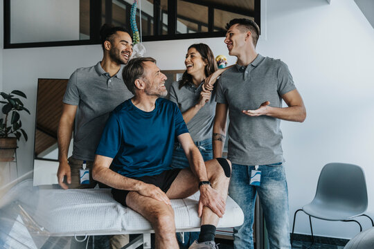 Cheerful male physical therapists standing behind patient at massage table