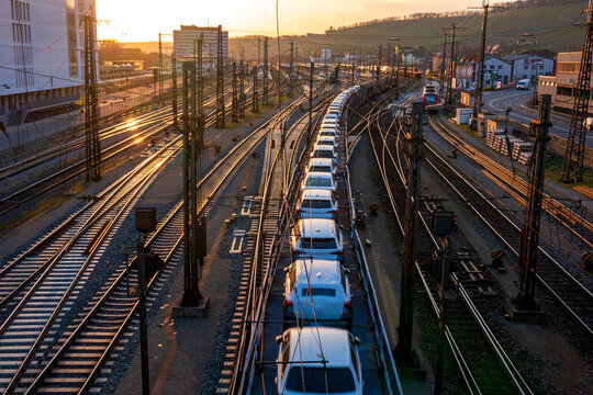 Germany, Bavaria, Wurzburg, Row od cars transported along city railroad tracks at sunset
