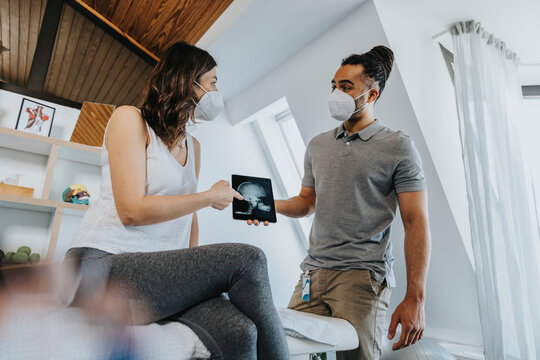 Female patient discussing over digital x-ray image with male physical therapist in practice during COVID-19