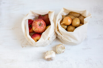 Apples and vegetables in cloth bags on white textured background