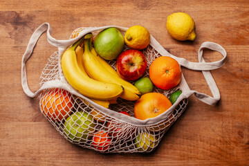Reusable cotton mesh bag with fresh fruits lying on wooden table
