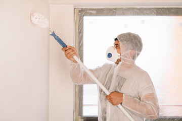 Man painting a white wall in the kitchen at home