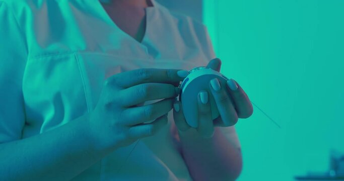 The female orthodontist is holding a ceramic model of a jaw and attaching a metal archwire to the braces and taking off the arch by using forceps.