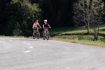 Woman and girl child riding mountain bikes on a country road in nature on a bright sunny summer day.