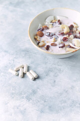 Bowl of granola with yogurt, nuts, cranberry and cocoanut. Sport supplements ( carnitine capsules ) in background. Bright stone  background. Copy space. 
