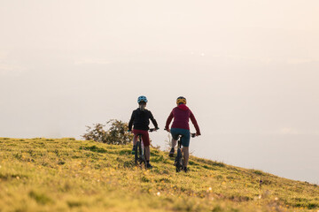 Obraz premium Mother and daughter cycling downhill with mtb bikes at a sunset.