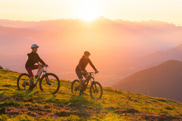 Fototapeta na wymiar Mother and daughter cycling uphill with mountain bikes at a sunset.