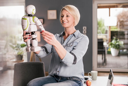 Smiling businesswoman holding model of robot while sitting on table at home office