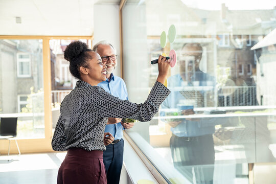 Smiling female professional writing on adhesive notes by mature male colleague at office