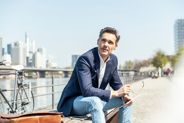 Thoughtful male entrepreneur looking away while sitting on bench during sunny day