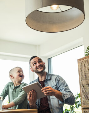 Smiling son sitting with father controlling pendant light through tablet at smart home