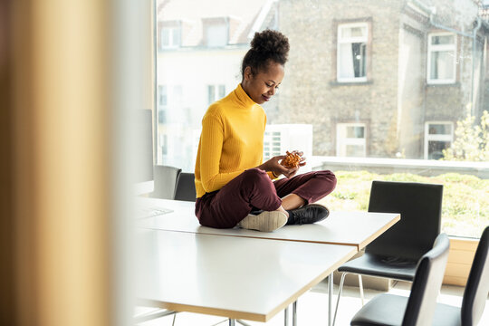 Businesswoman playing with puzzle cube while sitting cross-legged on desk at office