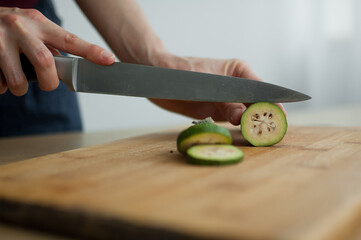 Obraz na płótnie Canvas Female hands is cutting a fresh green feijoa fruit on a cut wooden board. Exotic fruits, healthy eating concept