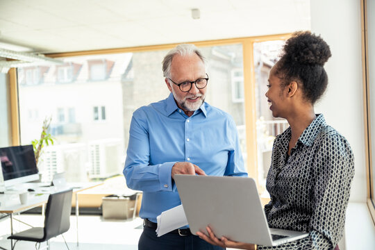 Smiling businessman discussing over laptop with female professional at office