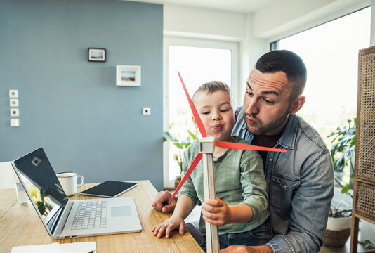 Male freelancer with son blowing wind turbine while playing at home