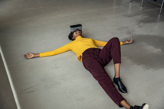 Woman wearing virtual reality headset lying on floor at office