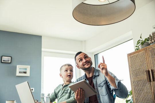 Man sitting with son pointing at pendant light in smart home