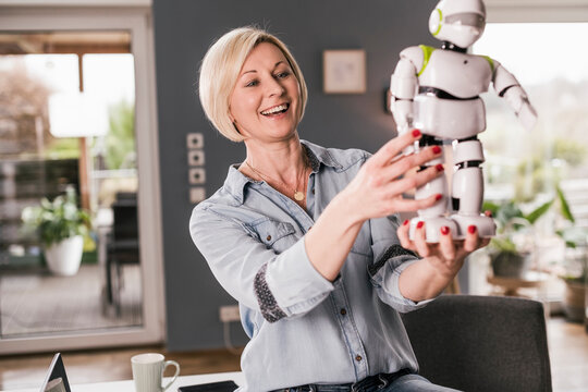 Cheerful female entrepreneur examining robot model while working at home