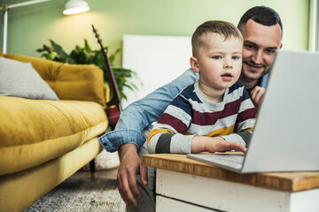 Smiling father looking at son using laptop in living room