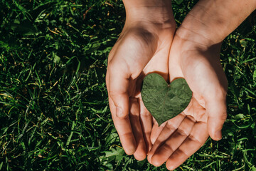 child holding a green leaf in the shape of a heart on a green background.concept of ecology,earth...