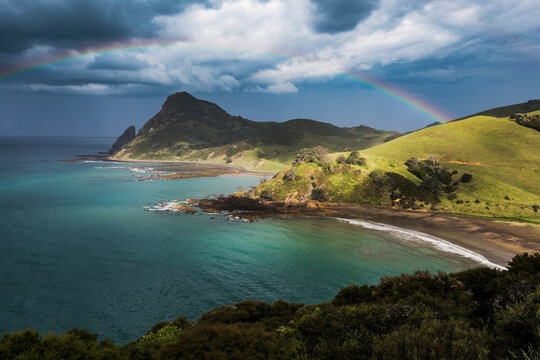 Rainbow arching against storm clouds gathering over coastline of Coromandel Peninsula