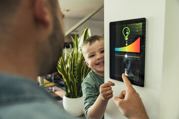 Smiling boy with father using tablet while adjusting lights at smart home