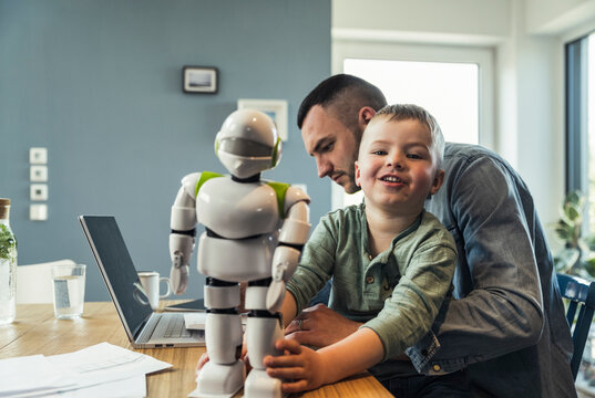 Smiling boy playing with robot while father working on laptop at home