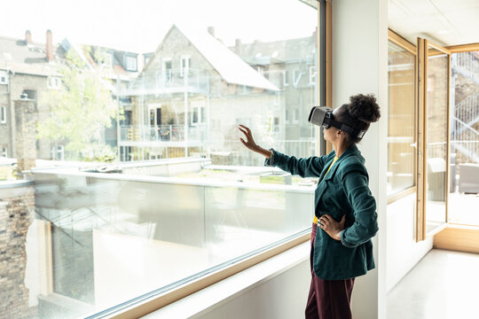 Businesswoman with hand on hip using wearable computer while touching glass at office