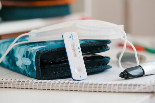 Rapid diagnostic test kit with protective face mask over pencil case at desk in school