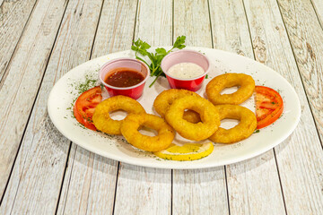 Fried squid accompanied by dipping sauces on a white table with parsley