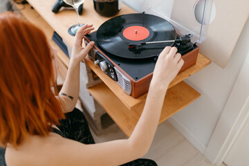 Unrecognizable woman turning on turntable with vinyl record at home