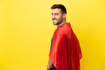 Young handsome caucasian man isolated on yellow background in superhero costume and doingposing...