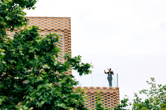 Lady in VR headset on balcony of building near trees